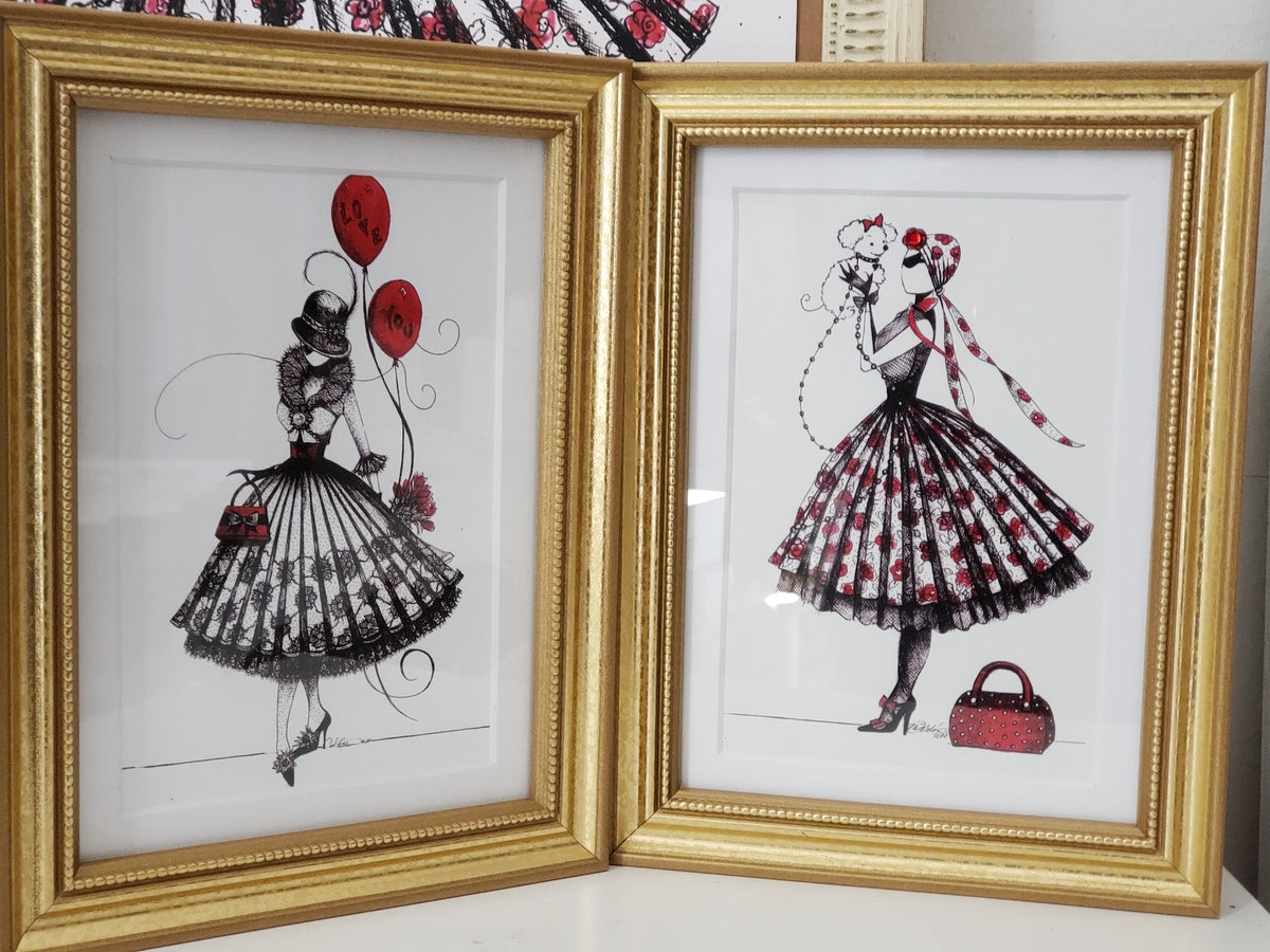 Two framed illustrations of the character MeowCleeva in a dress with red accents on a white dresser artwork by artist Martha Colón