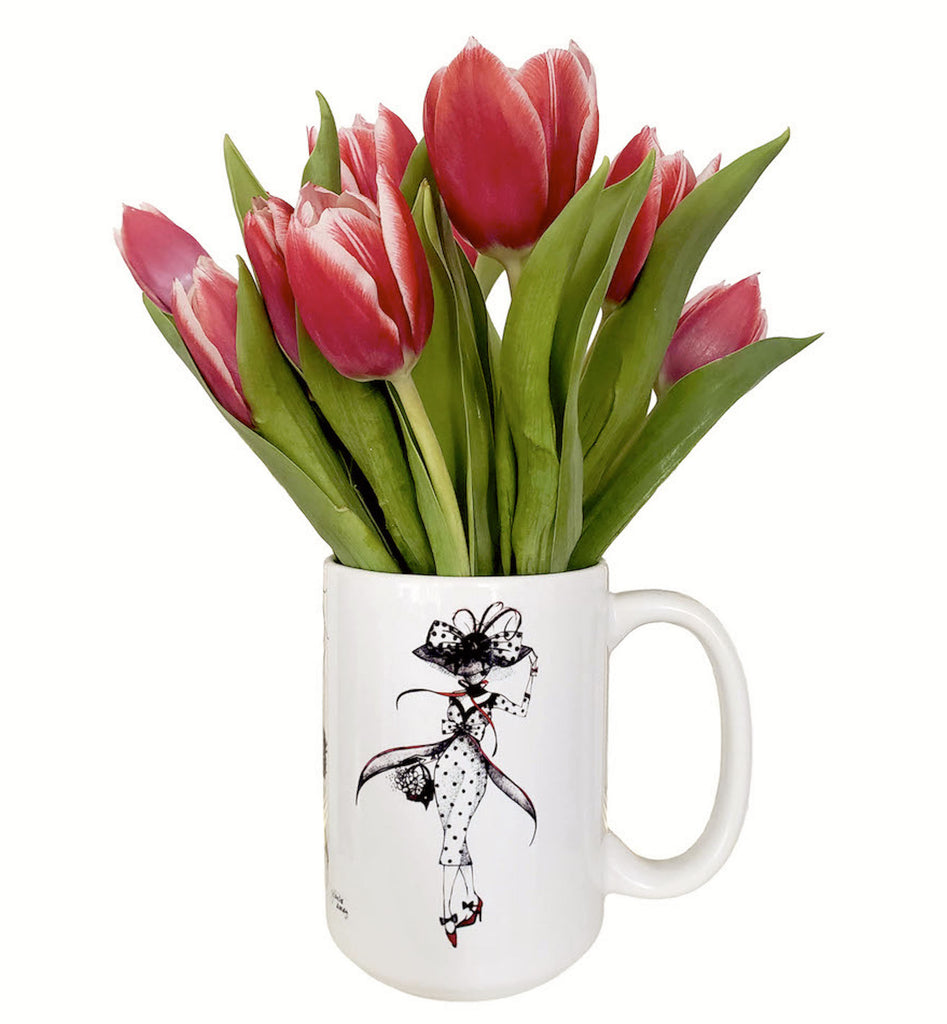 White mug with  fashionable ladies in custom dresses in vintage style. illustration  in black and red by Martha colon. Mug is  filled with  a petite bouquet from whole foods market of pink tulips and green leaves 
