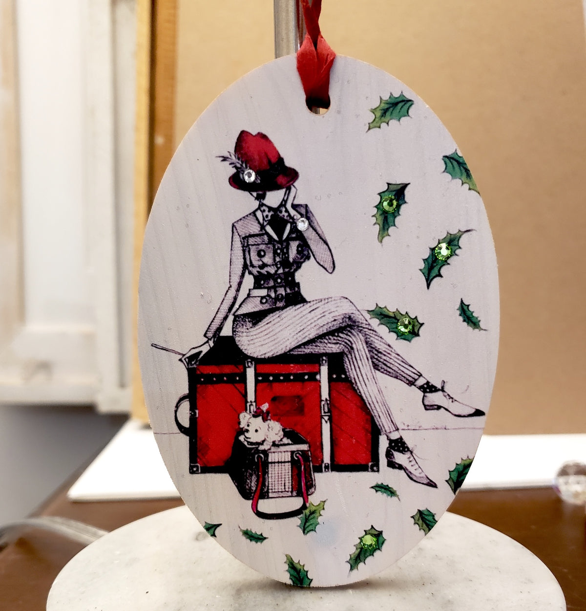 Hand painted wood ornament featuring MeowCleeva® seated on her red trunk with her little dog, adorned with Swarovski crystals. Holly border. One of a kind. $125.